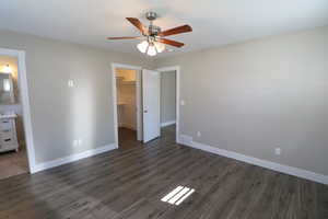 Unfurnished bedroom featuring dark wood-type flooring, a spacious closet, and a ceiling fan