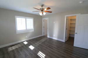 Unfurnished bedroom featuring a spacious closet, dark wood-type flooring, and ceiling fan
