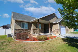 View of front facade with stucco siding, covered porch, a garage, and stone siding