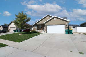 View of front of home featuring driveway, stucco siding, a garage, stone siding, and a front lawn