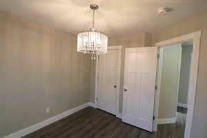 Unfurnished dining area featuring a chandelier and dark wood-style floors