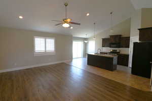 Kitchen with open floor plan, black appliances, an island with sink, light wood-type flooring, and recessed lighting