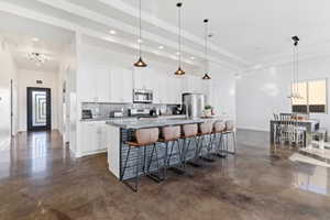Kitchen with pendant lighting, backsplash, white cabinets, a kitchen island with sink, and finished concrete floors
