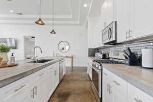 Kitchen with finished concrete flooring, stainless steel appliances, white cabinets, a tray ceiling, and hanging light fixtures