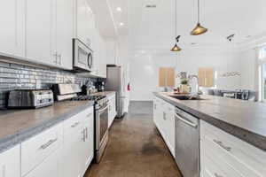 Kitchen featuring white cabinetry, finished concrete flooring, appliances with stainless steel finishes, hanging light fixtures, and recessed lighting