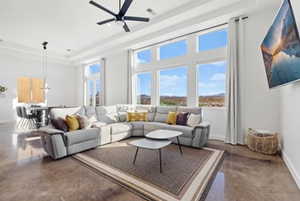 Living area with a raised ceiling, finished concrete flooring, and a ceiling fan
