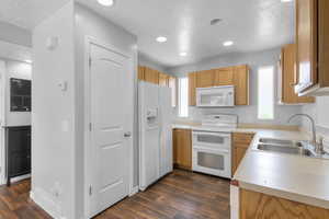 Kitchen with a textured ceiling, white appliances, dark wood-style floors, light countertops, and recessed lighting