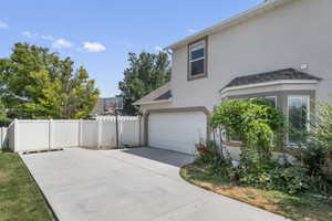 View of side of property with stucco siding, concrete driveway, a garage, and a shingled roof