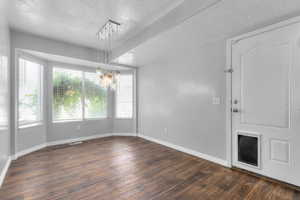 Empty room featuring a textured ceiling, dark wood-style floors, and a chandelier