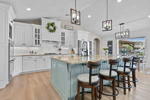 Kitchen with decorative light fixtures, arched walkways, tasteful backsplash, glass insert cabinets, and white cabinetry