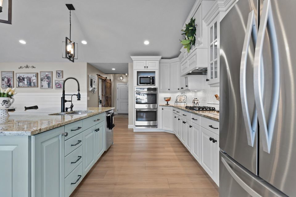 Kitchen featuring stainless steel appliances, white cabinetry, decorative light fixtures, light stone counters, and glass insert cabinets