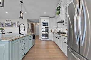 Kitchen featuring stainless steel appliances, white cabinetry, decorative light fixtures, light stone counters, and glass insert cabinets