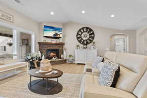 Living room with recessed lighting, light wood finished floors, a fireplace, lofted ceiling, and arched walkways