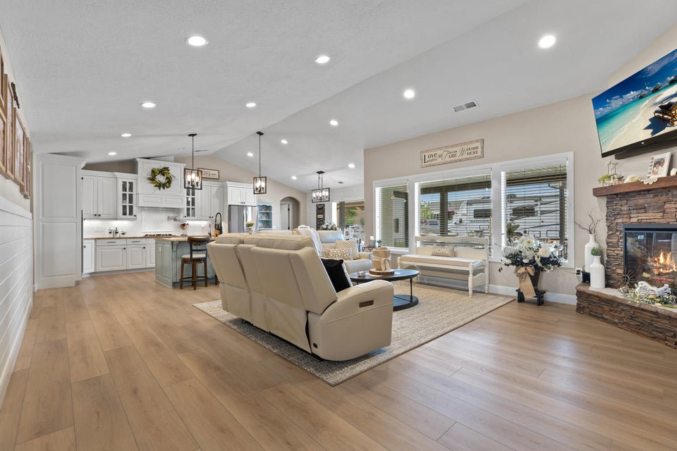 Living area featuring a stone fireplace, light wood finished floors, lofted ceiling, recessed lighting, and arched walkways