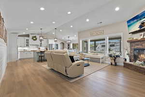 Living area featuring a stone fireplace, light wood finished floors, lofted ceiling, recessed lighting, and arched walkways