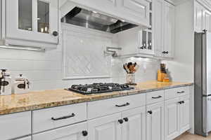 Kitchen featuring glass insert cabinets, light stone countertops, premium range hood, and backsplash