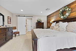 Bedroom with a barn door, wooden walls, light colored carpet, and recessed lighting