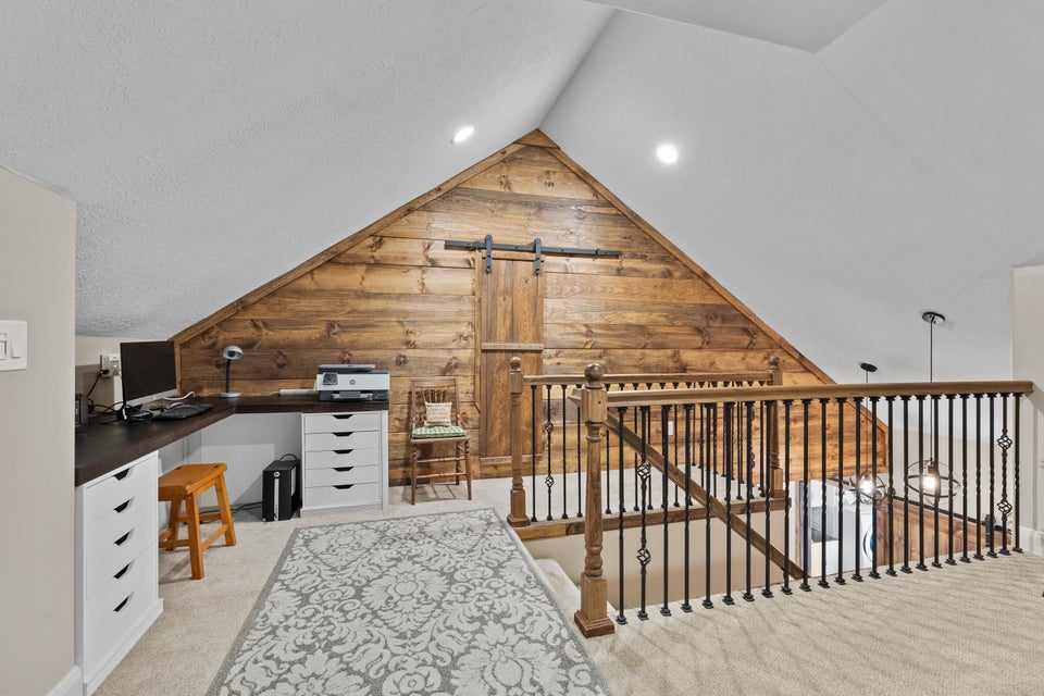 Unfurnished office featuring wood walls, light colored carpet, a barn door, lofted ceiling, and a textured ceiling