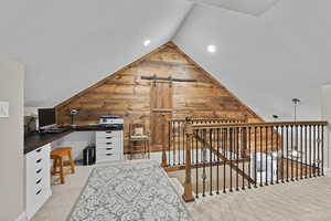 Unfurnished office featuring wood walls, light colored carpet, a barn door, lofted ceiling, and a textured ceiling