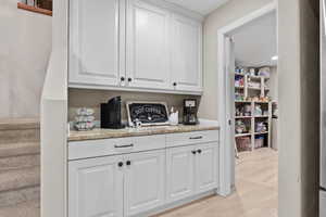 Bar area featuring white cabinets, light stone countertops, and stairway