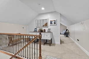 Office with vaulted ceiling, light colored carpet, and wood walls