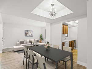 Dining area featuring a raised ceiling, light wood-style floors, and a chandelier