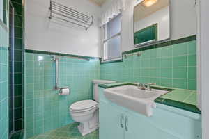 Full bathroom with tile walls, tile patterned flooring, wainscoting, vanity, and tiled shower