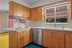 Kitchen featuring wallpapered walls, light countertops, appliances with stainless steel finishes, a peninsula, and brown cabinetry