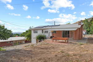Rear view of house featuring a patio area, roof mounted solar panels, a chimney, brick siding, and a shingled roof
