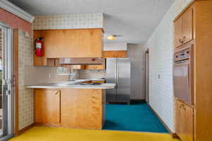 Kitchen with a textured ceiling, light countertops, appliances with stainless steel finishes, wallpapered walls, and a peninsula