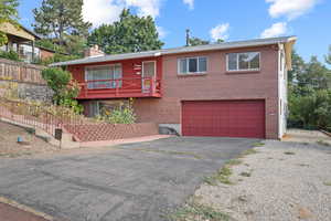 Bi-level home featuring a chimney, an attached garage, driveway, and brick siding