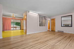 Spare room featuring light wood-type flooring, a chandelier, and a textured ceiling