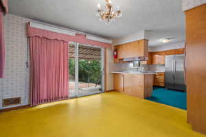 Kitchen with wallpapered walls, light countertops, freestanding refrigerator, a textured ceiling, and a chandelier