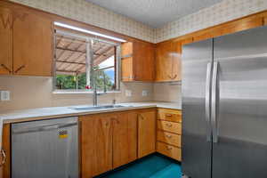 Kitchen with stainless steel appliances, light countertops, brown cabinetry, and a textured ceiling