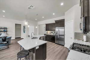 Kitchen with dark brown cabinets, stainless steel appliances, pendant lighting, light stone counters, and recessed lighting