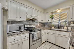Kitchen featuring stainless steel appliances, tasteful backsplash, light tile patterned floors, and under cabinet range hood