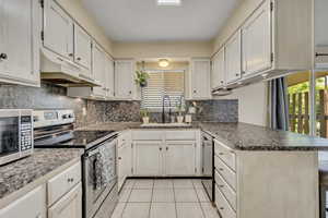 Kitchen with appliances with stainless steel finishes, a peninsula, under cabinet range hood, light tile patterned floors, and decorative backsplash