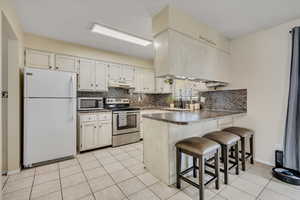 Kitchen with appliances with stainless steel finishes, a breakfast bar area, backsplash, a peninsula, and light tile patterned floors