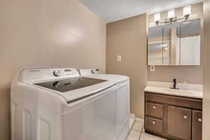 Laundry area featuring light tile patterned floors, a textured ceiling, washer and dryer, and cabinet space