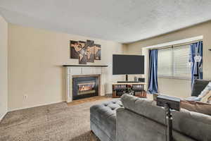 Living area featuring a tiled fireplace, a textured ceiling, and carpet