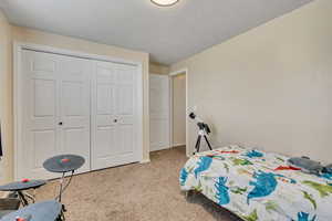 Bedroom featuring light colored carpet, a textured ceiling, and a closet