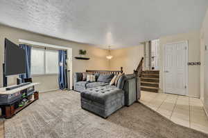 Living room featuring a textured ceiling, light carpet, stairs, and light tile patterned floors