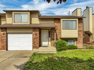 View of front facade with a garage, driveway, brick siding, and a front lawn