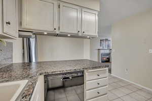 Kitchen with black dishwasher, a glass covered fireplace, and light tile patterned floors
