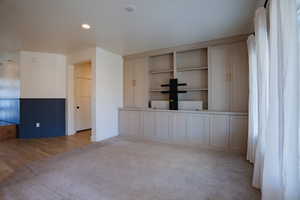 Unfurnished living room with light colored carpet, a wainscoted wall, light wood-style floors, and recessed lighting