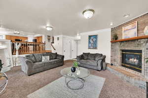 Living room featuring ornamental molding, carpet floors, a brick fireplace, a textured ceiling, and recessed lighting