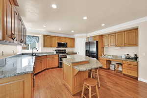 Kitchen with light wood-style flooring, a kitchen island, stainless steel appliances, crown molding, and light stone countertops