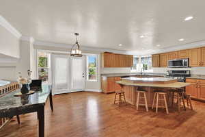 Kitchen with light wood-style flooring, crown molding, appliances with stainless steel finishes, a center island, and a kitchen bar