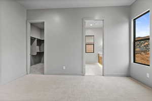 Unfurnished bedroom with a walk in closet, light colored carpet, and ensuite bath