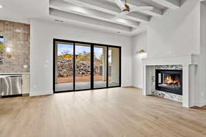 Unfurnished living room featuring a fireplace, a ceiling fan, light wood-style floors, and beam ceiling